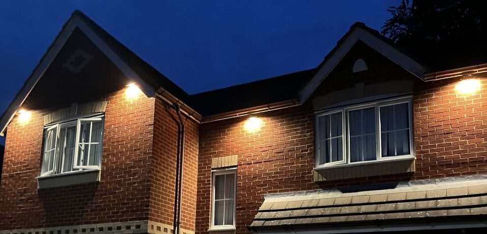 A brick house at dusk with soffit downlights lit along the eaves