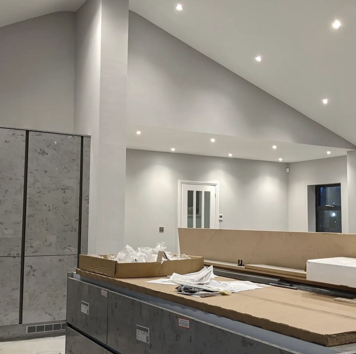 A new open-plan kitchen with downlights on, units still being fitted