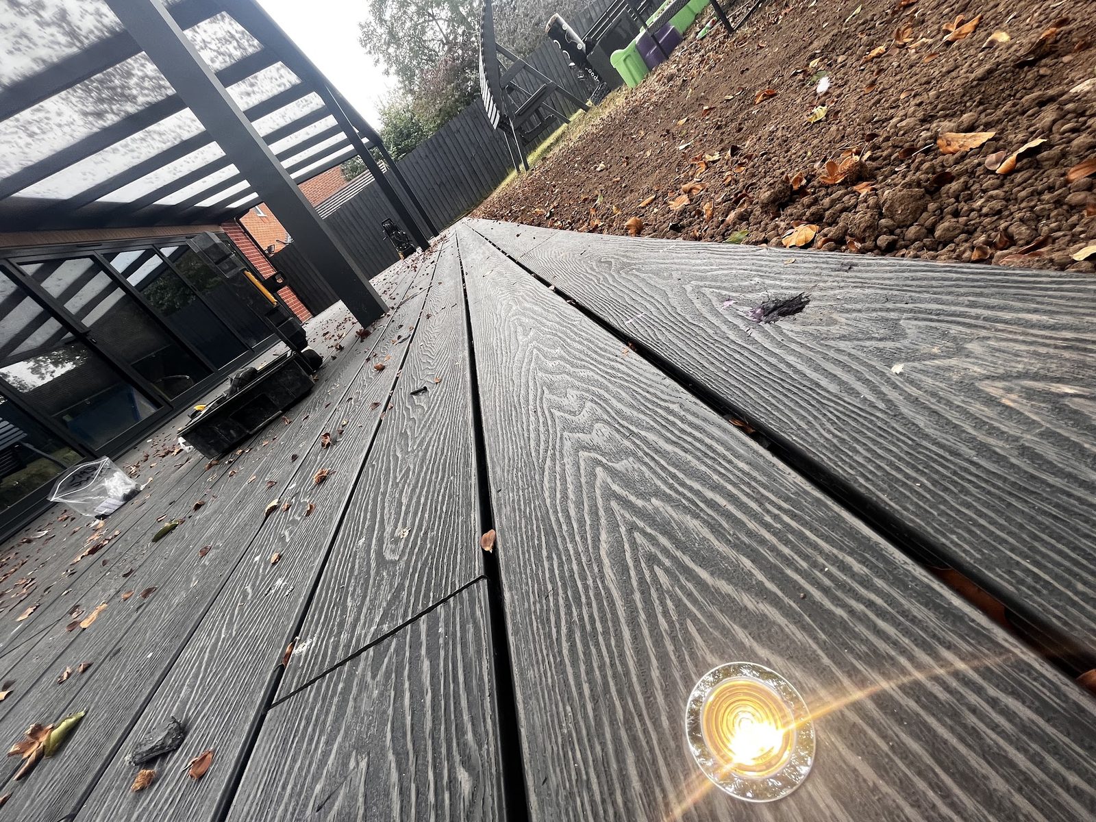 A lit LED light set into garden decking beside a pergola